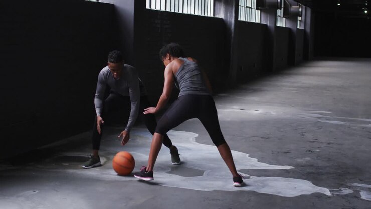 Afroamerikanischer Mann und afroamerikanische Frau, die in einem leeren Gebäude Basketball spielen.