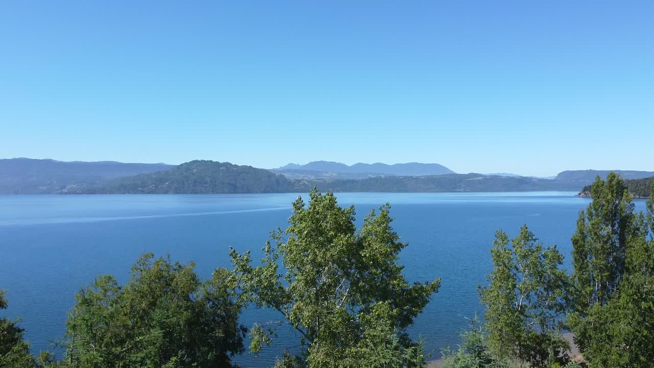 arboles rodean lago azul en el sur de 칠레, montañas verdes adornan el paisaje