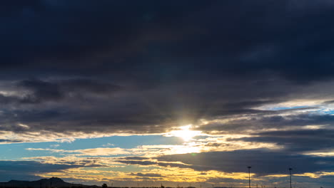 sunrise over horizon with mountains and light poles silhouetted against the golden sun and darkened clouds blowing in the wind - time lapse