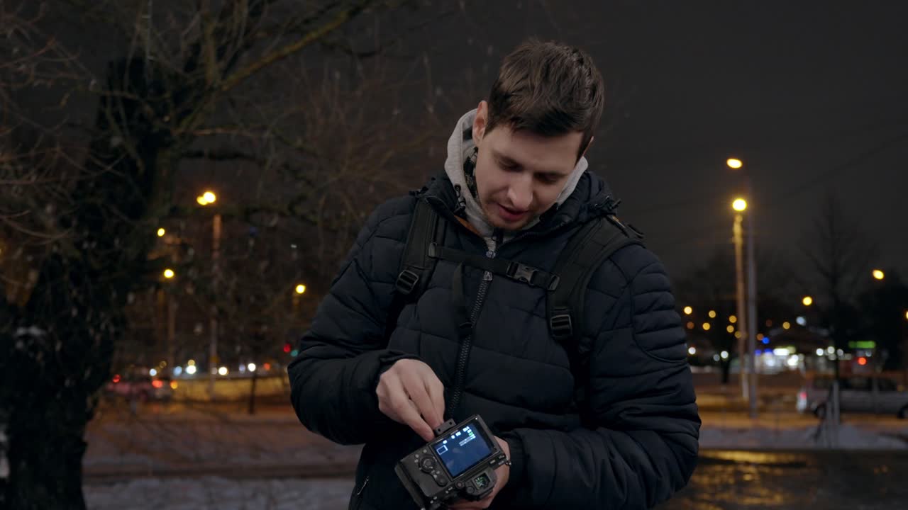 Young backpacker photographer adjusting digital camera gear at night in city outdoors