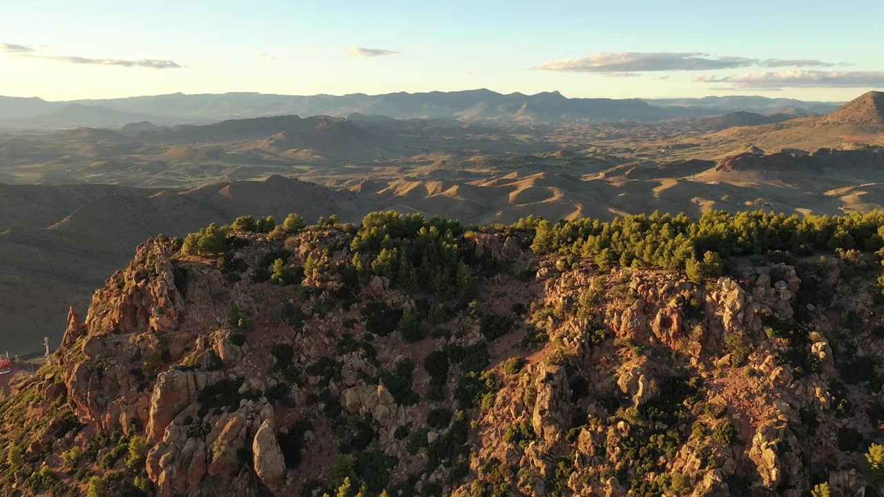 Volo cinematografico aereo con drone su una scarpata montuosa rocciosa e aspra, illuminata dalla calda luce dorata del tramonto nell'Atlante Medio, Marocco, ideale per progetti di documentari di viaggio, avventura e natura.