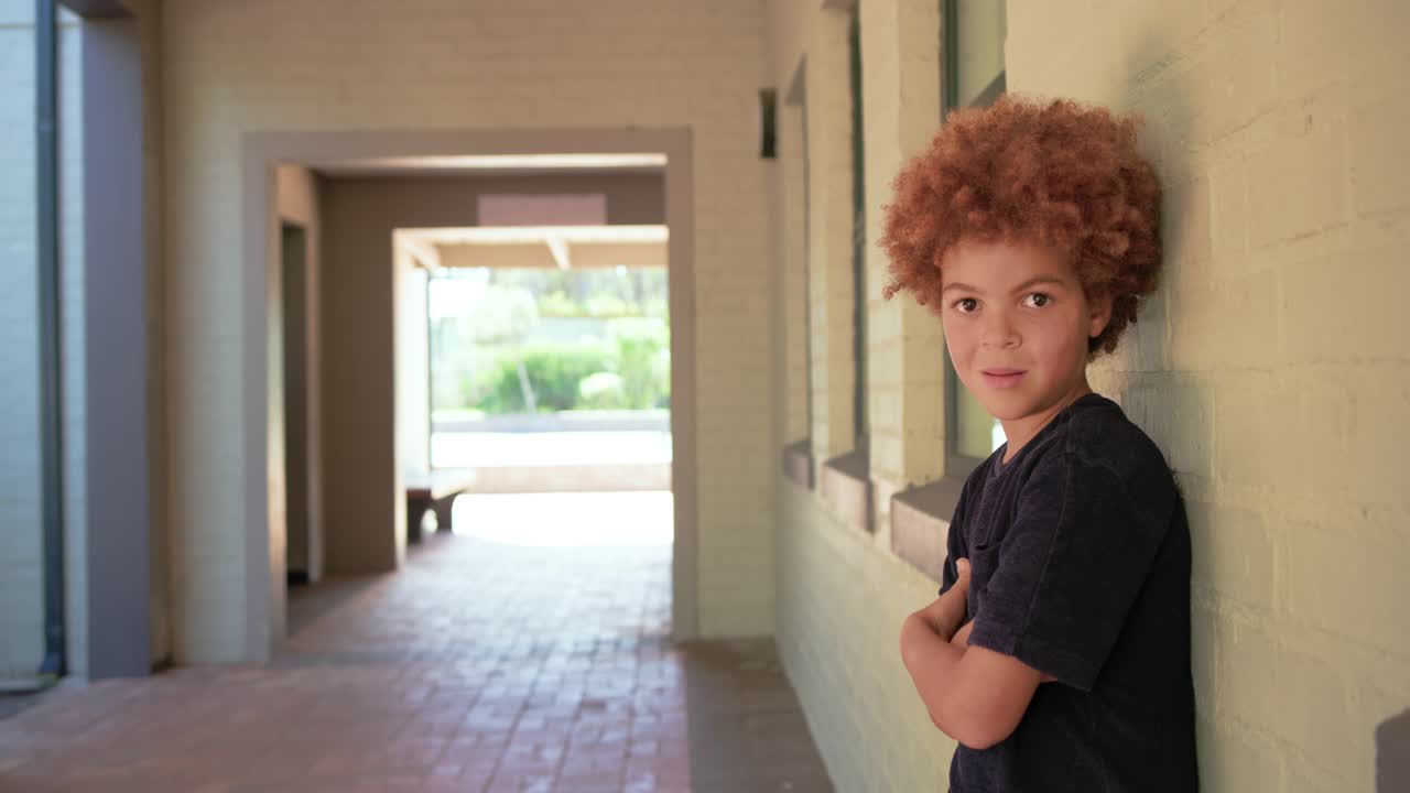 Boy leaning against brick wall in corridor turning toward approaching camera smiling, copy space