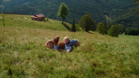 family rest green grass mountain meadow. joyful parents children lying ground.
