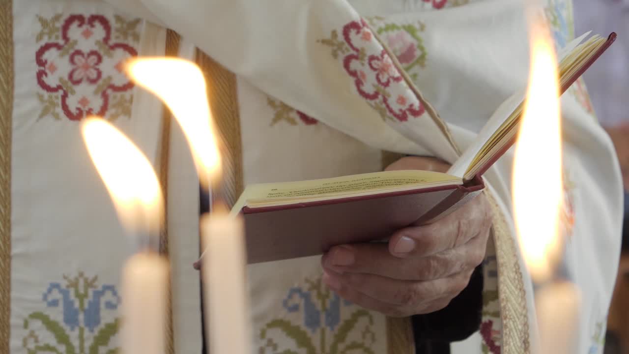 Close-up of a priest's hands holding religious book with lit candles in the foreground