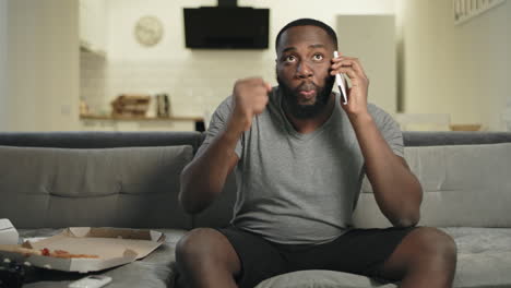 black man eating pizza in front of tv. male fan commenting match results