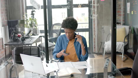 African-american-casual-businessman-sitting-at-desk-using-smartphone-and-laptop-at-home,-slow-motion