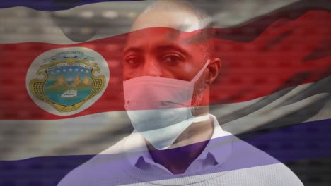 animation of flag of costa rica waving over african american man wearing face mask in city street