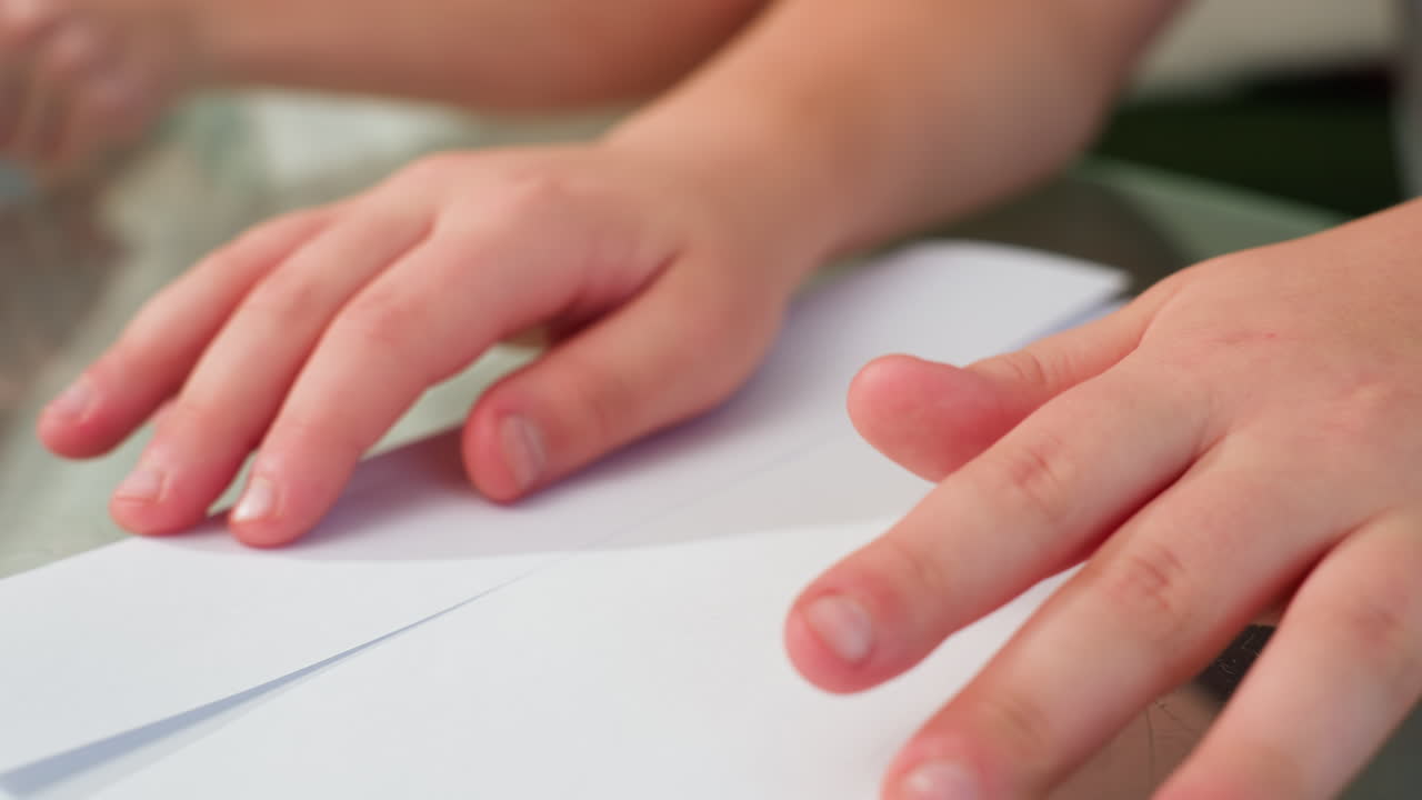 Close-up hand view of two kids engaged in crafting with paper, carefully creating paper craft on table, focusing on neatness and precision