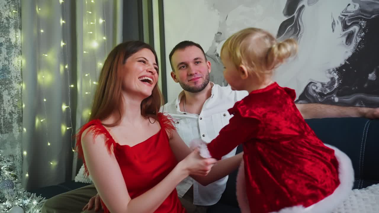 Family wearing matching red outfits joyfully playing with young daughter dressed in Santa Claus costume, sharing warm moments during festive Christmas eve celebration at home