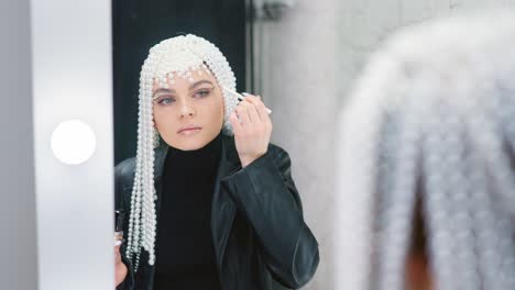 woman with pearl headpiece applying makeup in mirror