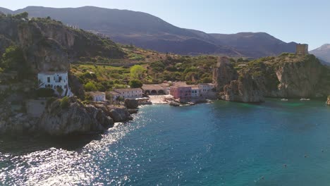 aerial drone pulling back to reveal rocky sicilian coast and tonnara di scopello under summer sunlight