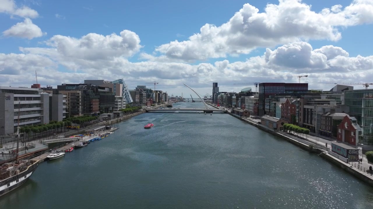 Rüzgarlı bir yaz gününde kamera, Liffey Nehri boyunca modern rıhtımların, ikiz yaya köprüsünün ve Samuel Beckett Köprüsü'nün yanından süzülüyor.