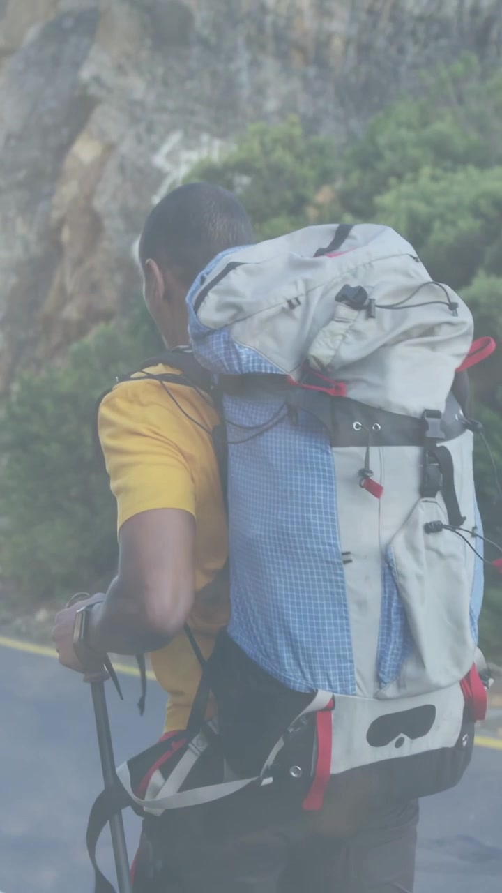 Video verticale: Escursionista che entra da sinistra, impugnando un bastone e regolando lo zaino mentre percorre una strada sulla scogliera.