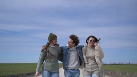 two young girls and a young boy walk happily and embraced along a road with their backs to each other.