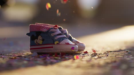 buntes konfetti, das auf babyschuhe fällt, hinterleuchtet mit warmem licht in zeitlupe