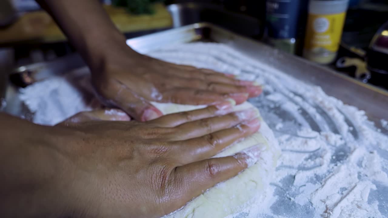 close up view of African american woman's hands kneading pizza dough in a silver pan in slow motion