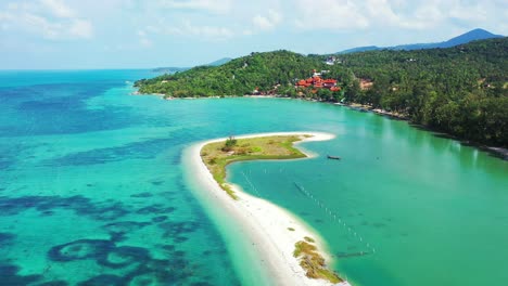 touristic village on coastline of tropical island with lush vegetation in front of calm turquoise lagoon surrounded by white sandy stripe in koh phangan, thailand