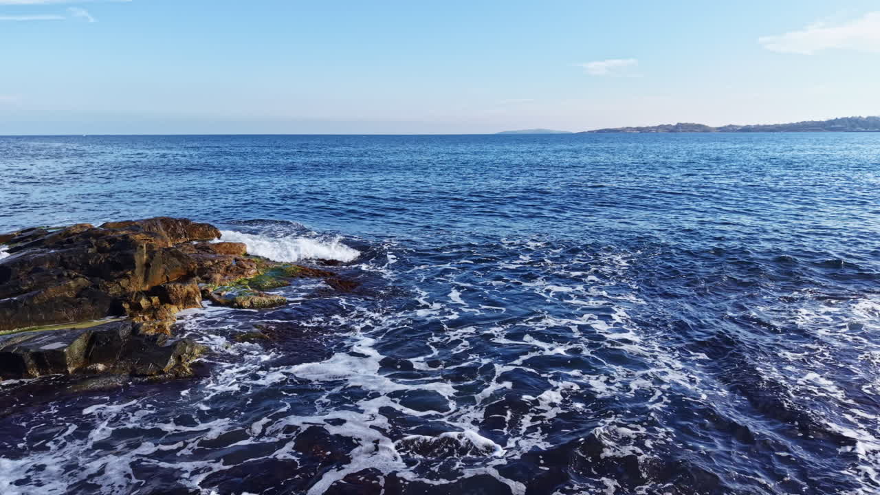 Levende havlandskap som viser bølger som slår mot robuste steiner på en solrik ettermiddag nær en rolig strandlinje