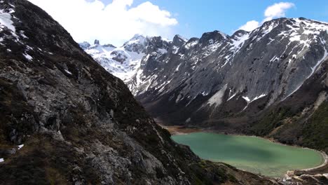 Drone-shot-flying-along-the-mountainside-to-reveal-the-Laguna-Esmeralda-near-Ushuaia,-Argentina-and-the-snow-covered-Andes