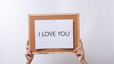 woman's hand shows the paper on board with the word i love you in white studio background with copy space