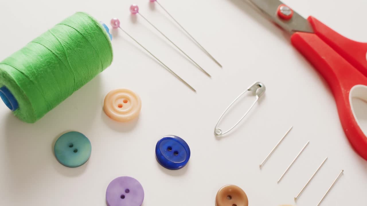 Video of scissors, buttons, pins and cotton reels arranged on white background