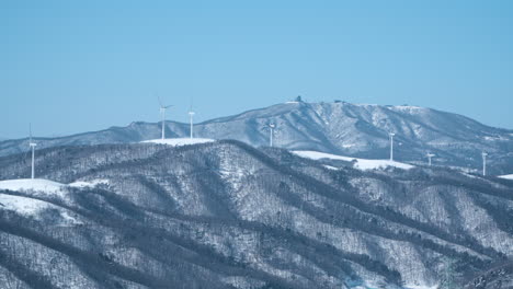 wind turbine farm on snow capped mountain range peaks spinning at daegwallyeong sky ranch, south korea