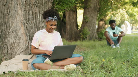 mujer afroamericana alegre usando una computadora portátil en el parque