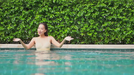 an excited asian woman in a swimming pool splashing water with her hands, slow-motion