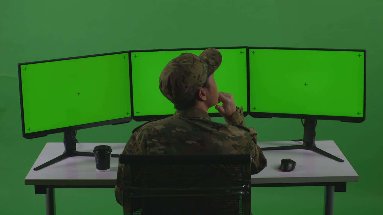 soldado en una estación de trabajo de computadora con monitores de pantalla verde
