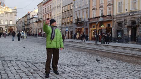 Senior-man-grandfather-tourist-is-making-online-video-call-with-smart-phone-in-winter-city-center