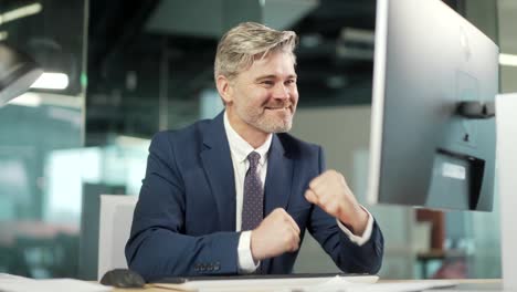 successful mature businessman wearing suit sitting at desk with laptop in office. portrait of a confident mid age gray hair male in the workplace working at a computer