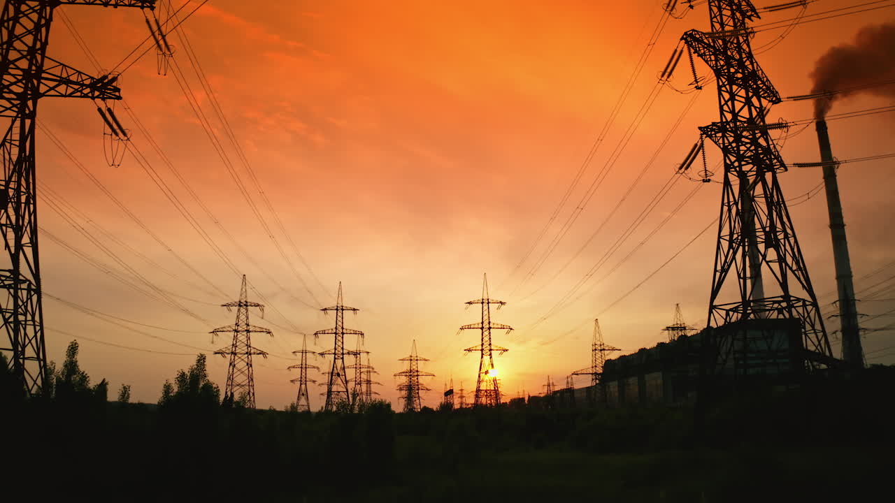 Transmission lines under red evening sky. High-voltage electric towers with wires in nature at beautiful sunset. Power lines against the backdrop of setting sun.