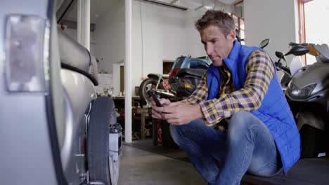 mecánico masculino usando teléfono móvil en el garaje de reparación de motocicletas 4k