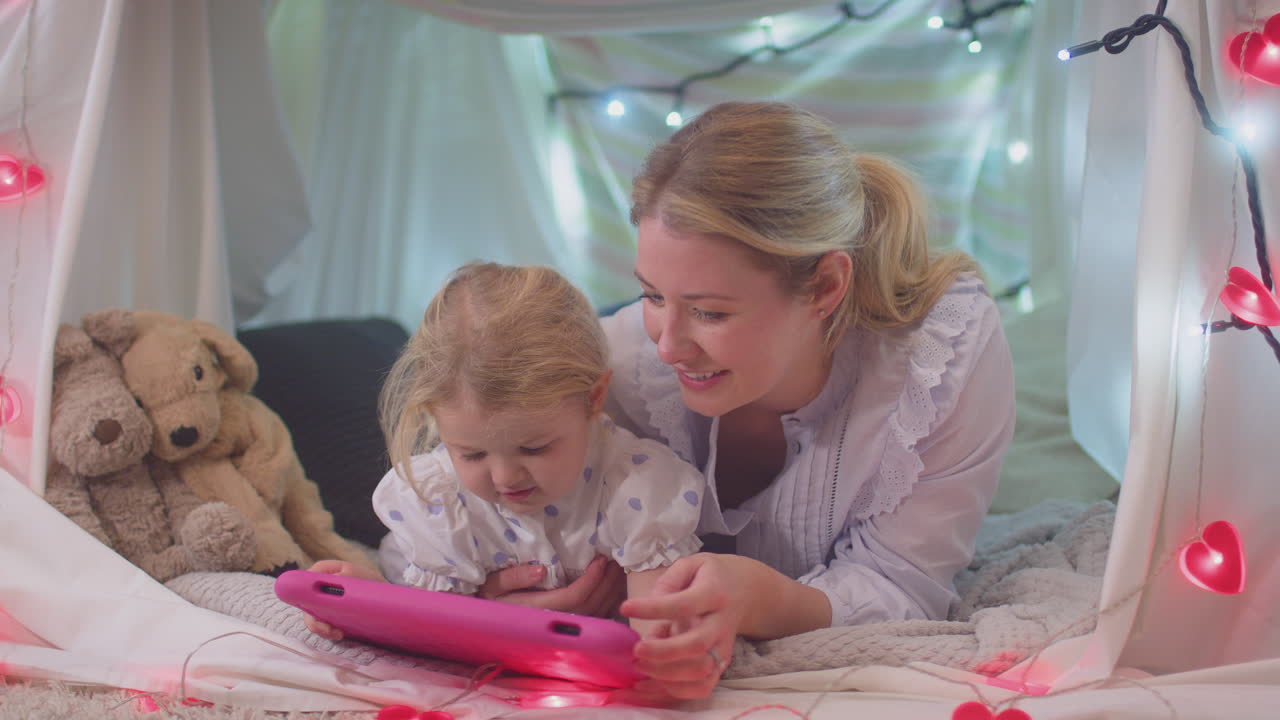 Mother and young daughter with digital tablet in homemade camp in child's bedroom at home - shot in slow motion