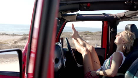 joven mujer caucásica se relaja en un coche en un viaje por carretera, los pies en el tablero