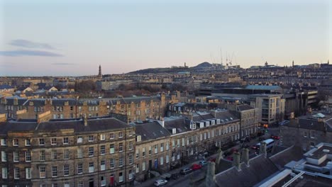 drone footage of edinburgh’s classic architecture, urban skyline, and distant hills during sunset. captures old buildings, construction cranes, and soft light over the cityscape. scotland