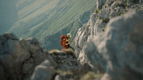 hiker descending on rope into the valley, green fields in the back, rocks in foregroud