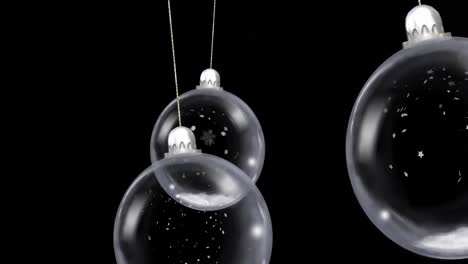 animation of christmas baubles dangling with snow falling on black background