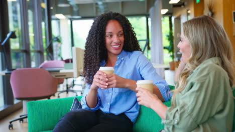 Businesswomen-With-Coffee-Having-Informal-Meeting-In-Breakout-Seating-Area-Of-Modern-Office