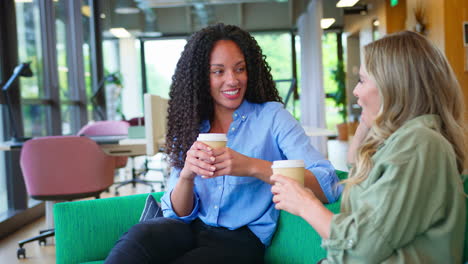 businesswomen with coffee having informal meeting in breakout seating area of modern office
