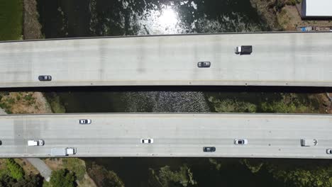 overhead shot of two bridges busy with cars on calm lagoon water, birds flying over peacefully, san mateo, california