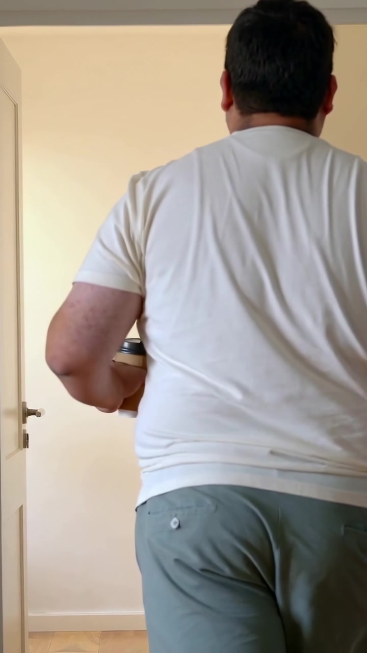 Video verticale: Uomo che cammina con maglietta chiara che tiene una tazza con coperchio che entra in una stanza di casa dopo che la porta si apre