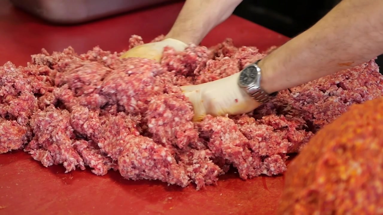 Boucher mélangeant de la viande hachée sur une planche à découper rouge