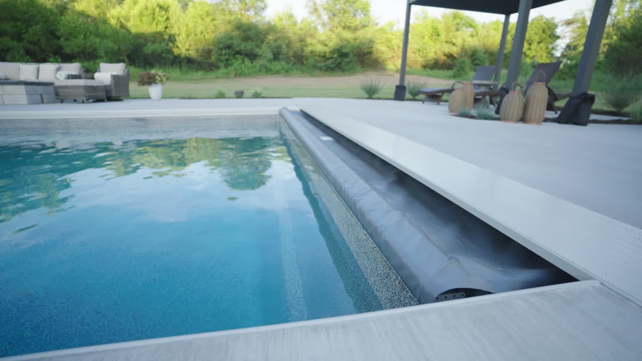 Fiberglass backyard pool with retracted cover and shaded lounge on sunny day
