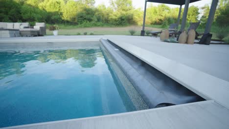 fiberglass backyard pool with retracted cover and shaded lounge on sunny day
