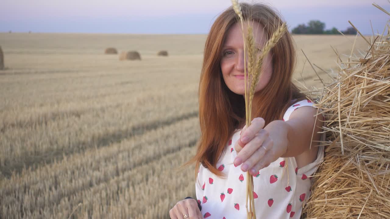 retrato al aire libre de una hermosa joven sonriente cerca de la bala redonda de heno en un campo de trigo