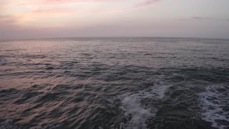 Drone-flying-over-rocky-pier-and-water-ocean-surface-at-sunset