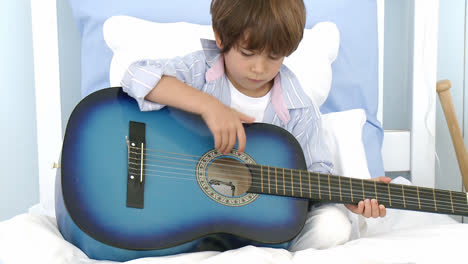 little boy playing guitar on bed