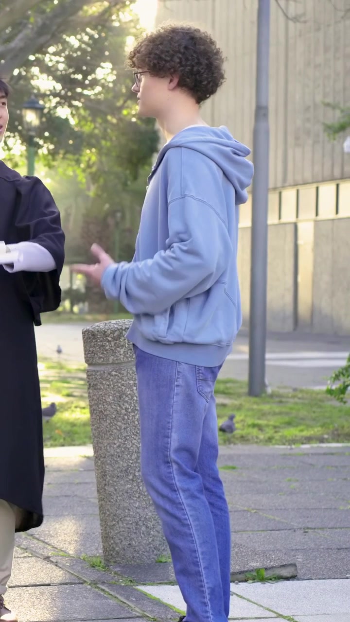Video verticale: Uomo con felpa con cappuccio che entra nel campus dopo un ingresso in toga da sinistra, ricevendo un diploma arrotolato.