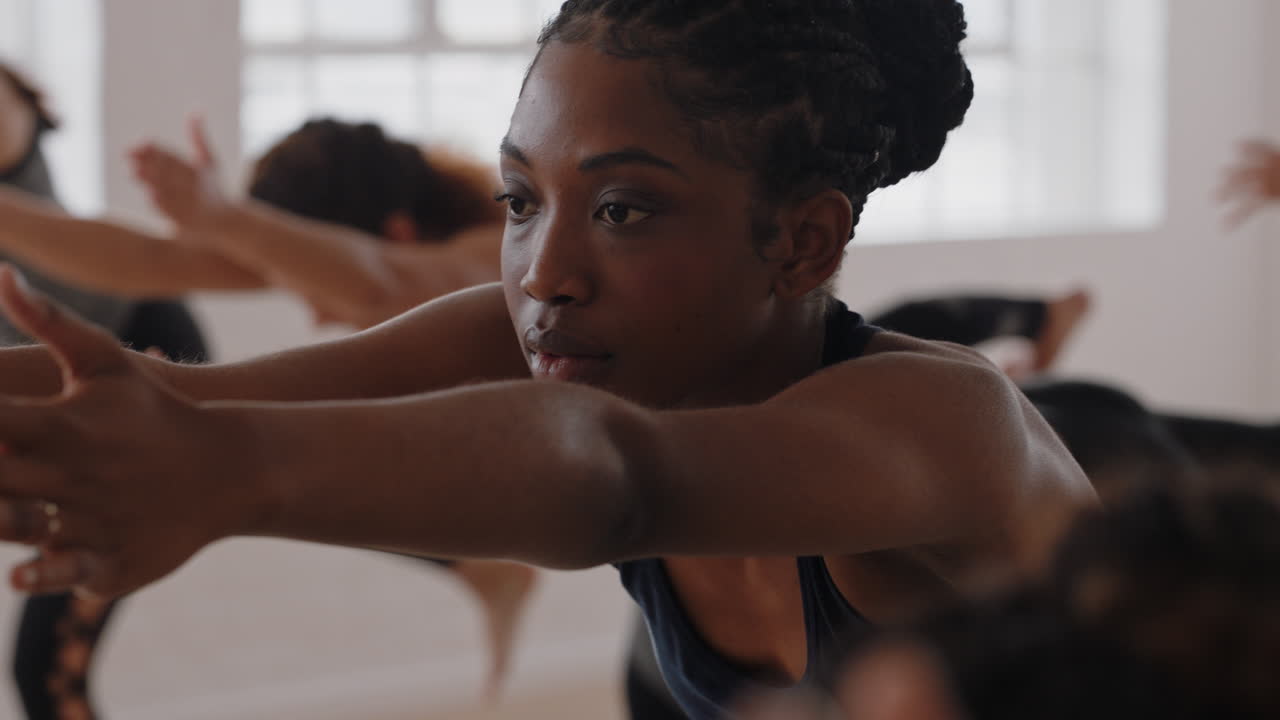 beautiful african american yoga woman practicing warrior pose meditation with group of multiracial women enjoying healthy lifestyle exercising in fitness studio